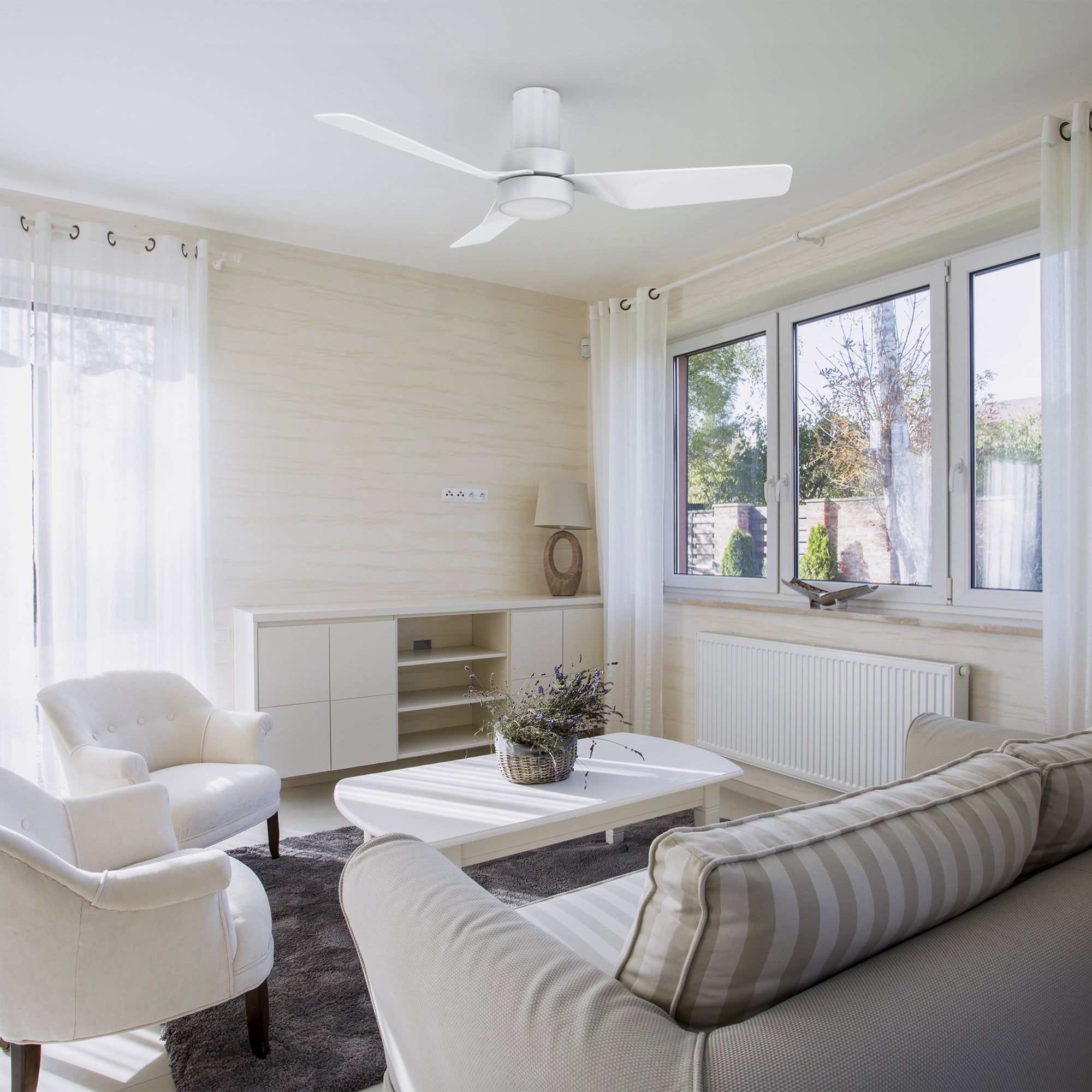 A modern and minimalist living room featuring the Barnet 44-inch flush mount smart ceiling fan in a sleek white finish. The fan has three blades and an integrated LED light, providing both illumination and air circulation. Controlled via remote, it seamlessly blends with the bright and airy decor of the space.