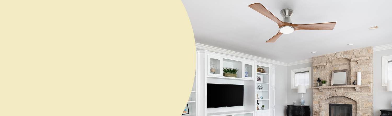 Living room banner with a modern ceiling fan featuring wooden blades and an LED light, mounted on a white ceiling at the top. The background includes gray walls, a white bookshelf with a black TV on the left, and a stone fireplace with decorations on the right. The lower section has a light yellow background.