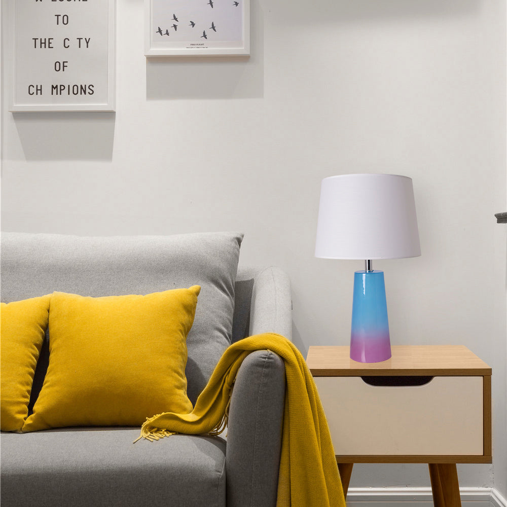 Carro Smafan Rosemary table lamp with white lampshade and ombre base placed on a modern wooden side table next to a gray sofa with a yellow throw pillow and blanket.