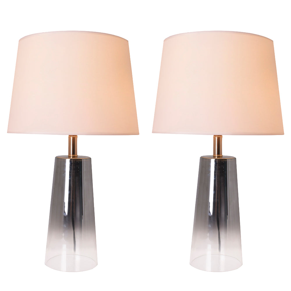 A pair of Carro Smafan Rosemary Table Lamps, 25 inches tall, with Chrome Grey Ombre finish and white shades, placed on nightstands in a bedroom. The lamps provide warm lighting, enhancing the room&