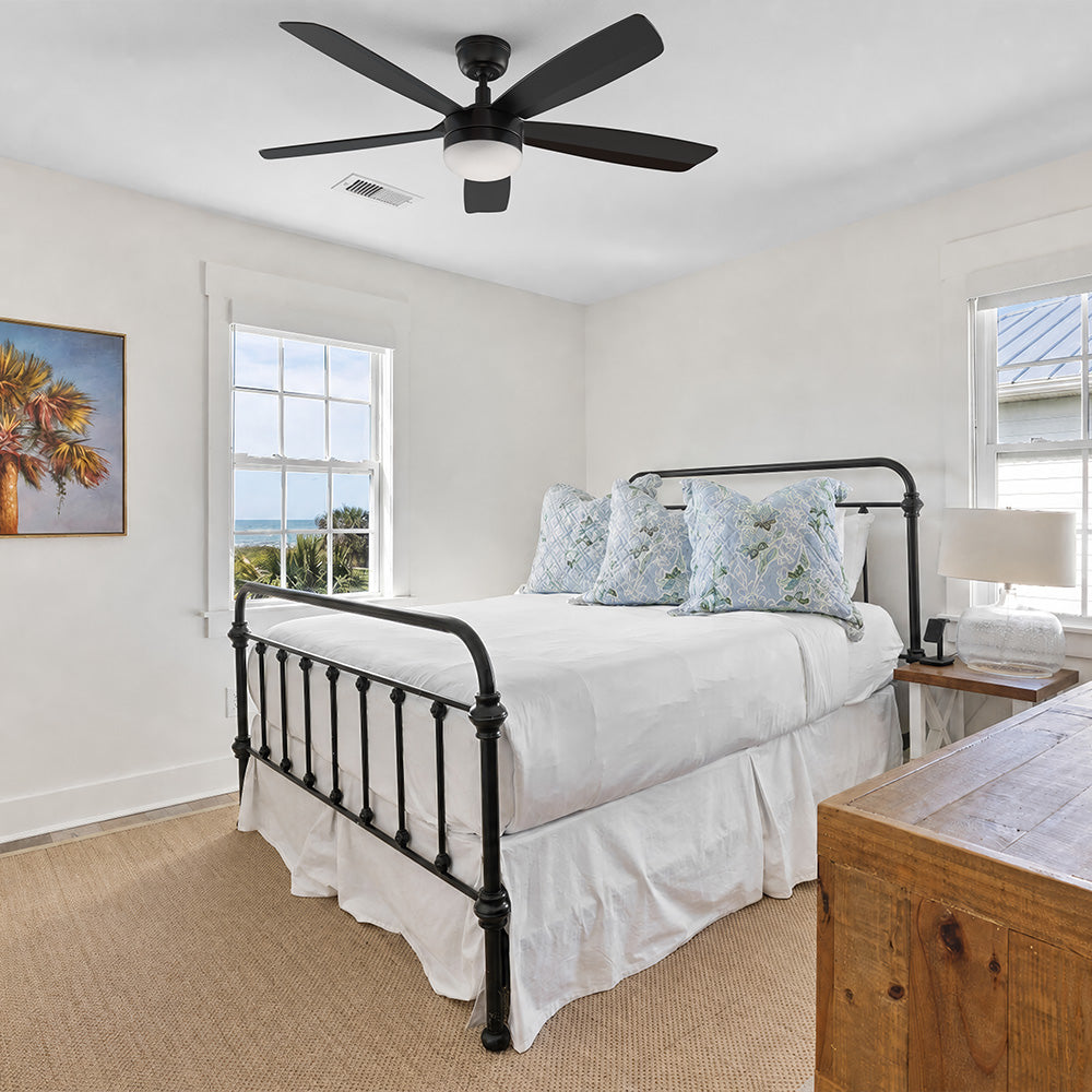 A stylish 52-inch black ceiling fan with a central light fixture installed in a modern bedroom with minimalist decor, featuring a low platform bed and large windows.