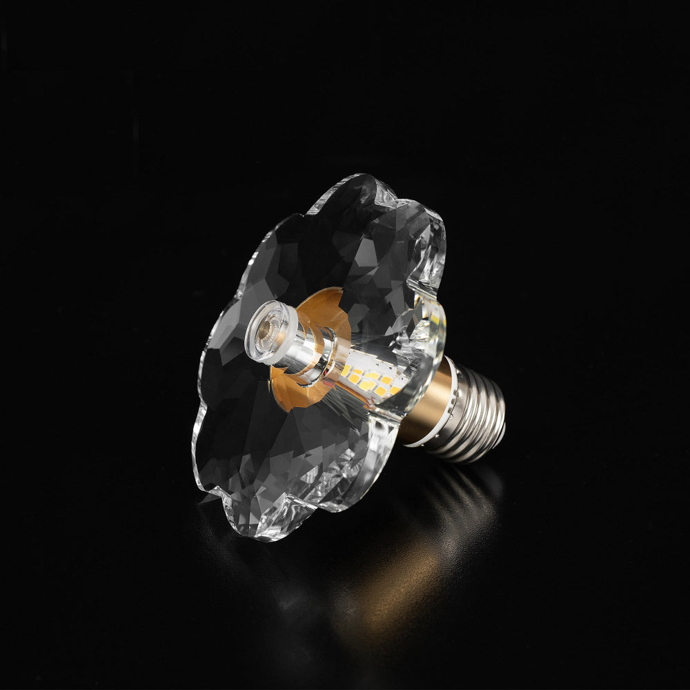 Clear crystal LED bulb with a faceted flower shape design and brass gold base collar, shown in a tilted product close-up view.