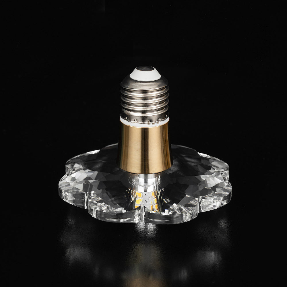 Decorative LED light bulb with a large flower-shaped faceted crystal design and gold metal base collar over a black background.