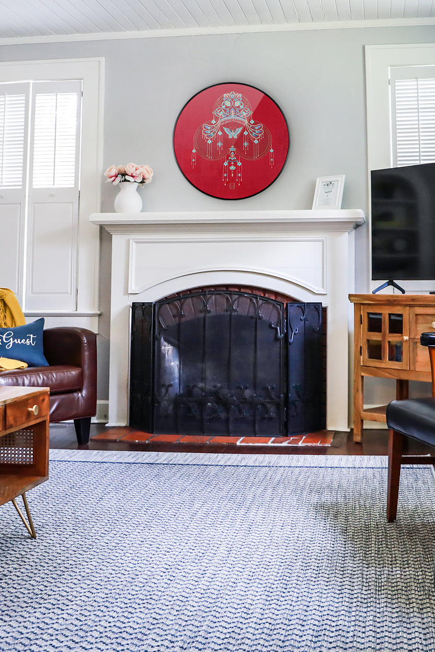 An embroidered wall artwork of a phoenix crown is placed above the fireplace in the modern living room.