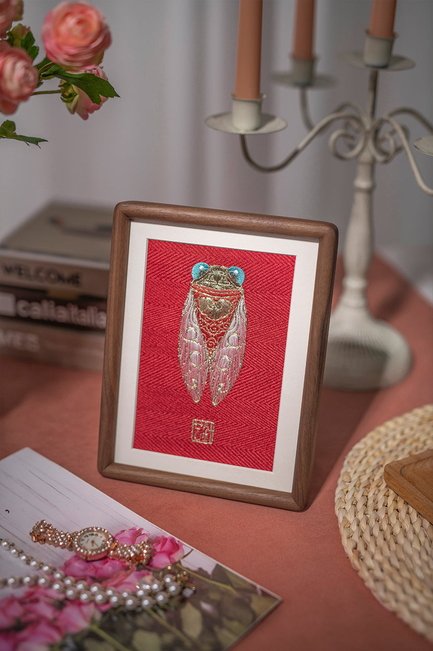 An embroidered artwork of golden cicadas, paired with artificial flower pink ranunculus, a pearl necklace, a gold watch, and a five-head candlestick holder with champagne-colored candles are quietly placed on the desk.