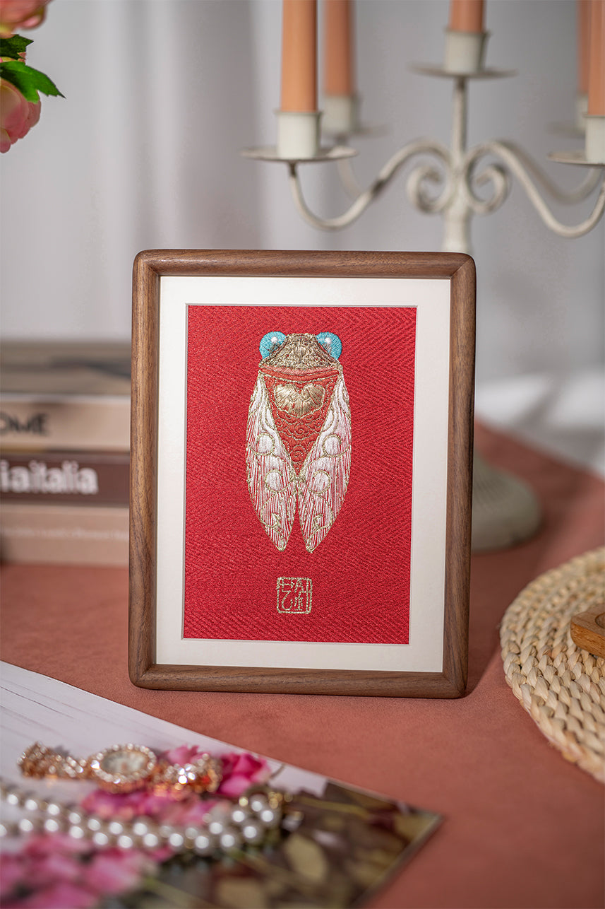 The golden Cicada embroidery artwork, paired with a five-head candlestick, pink flowers, and jewelry, is quietly placed on top of a wood-grain table