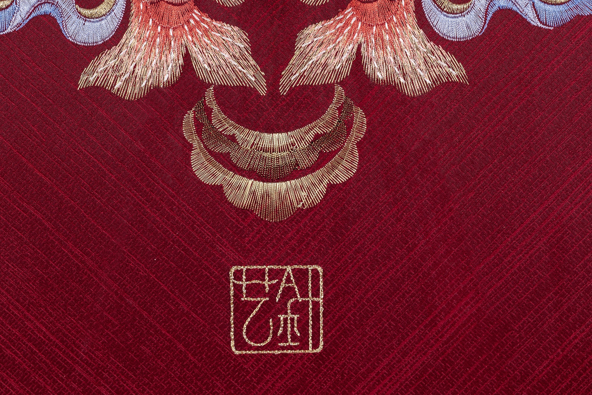 An embroidered work of art on a red background with two koi carp and a door handles with Oriental art and culture embroidered beneath the koi.
