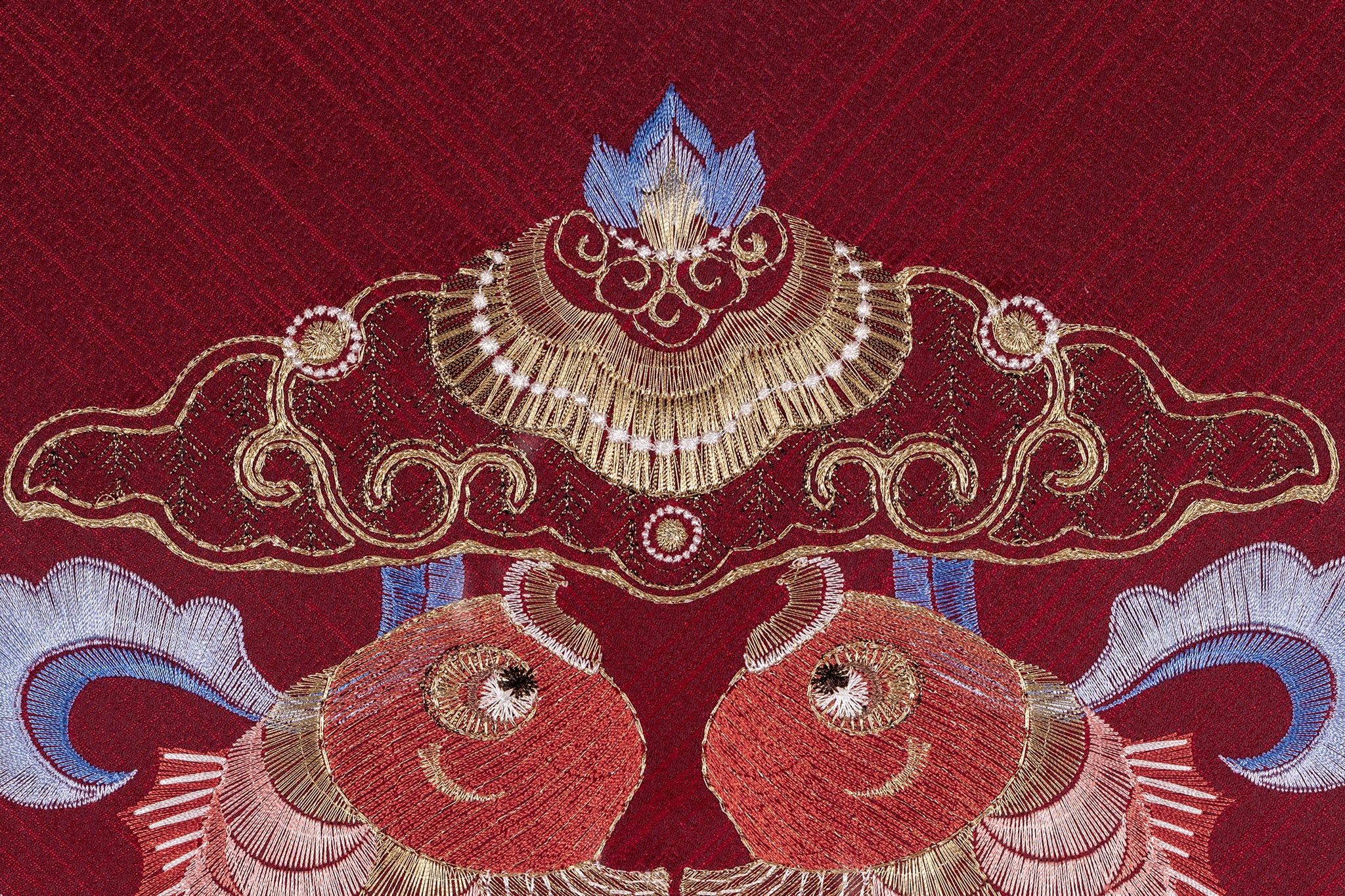 An embroidered work of art with a red background, embroidered with two koi carp, and a small lotus bud on the top of the carp.