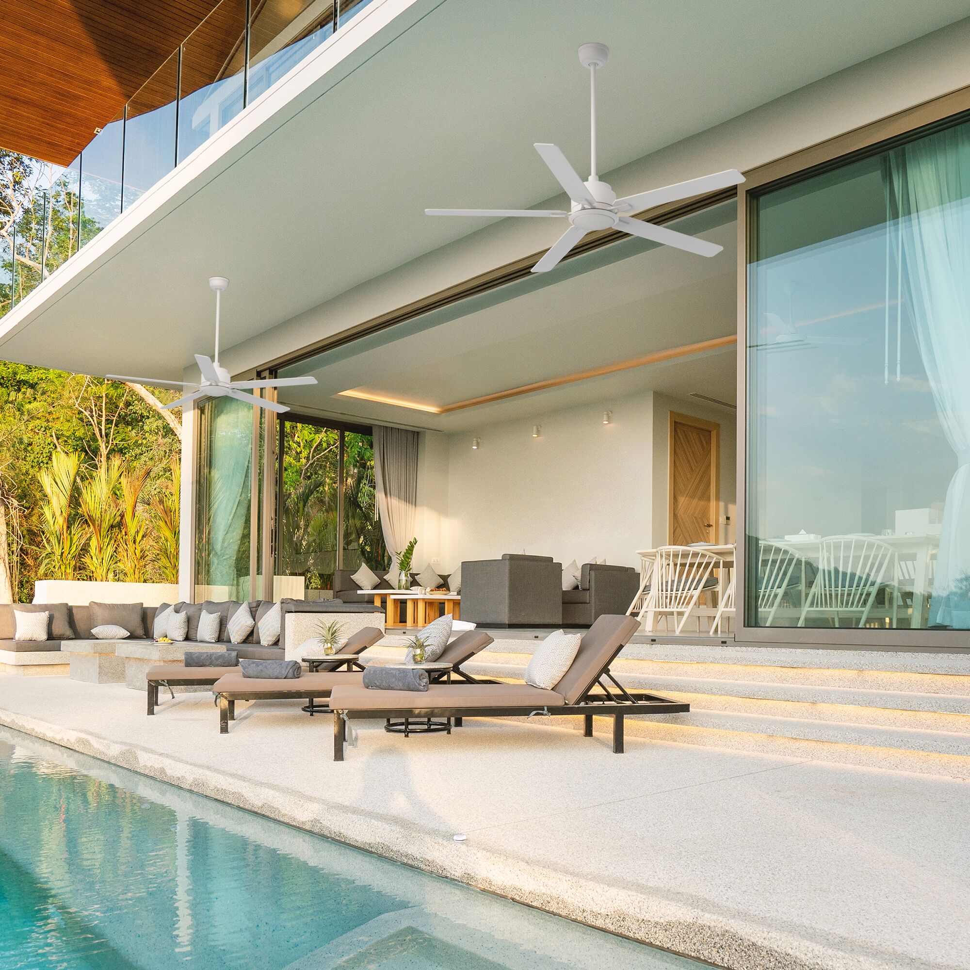 Outdoor patio featuring two smart ceiling fans in white with integrated LED light and remote control functionality. These modern 60-inch ceiling fans have a sleek 5-blade design and are mounted under a covered terrace by a swimming pool, providing quiet and efficient airflow for indoor-outdoor living spaces.