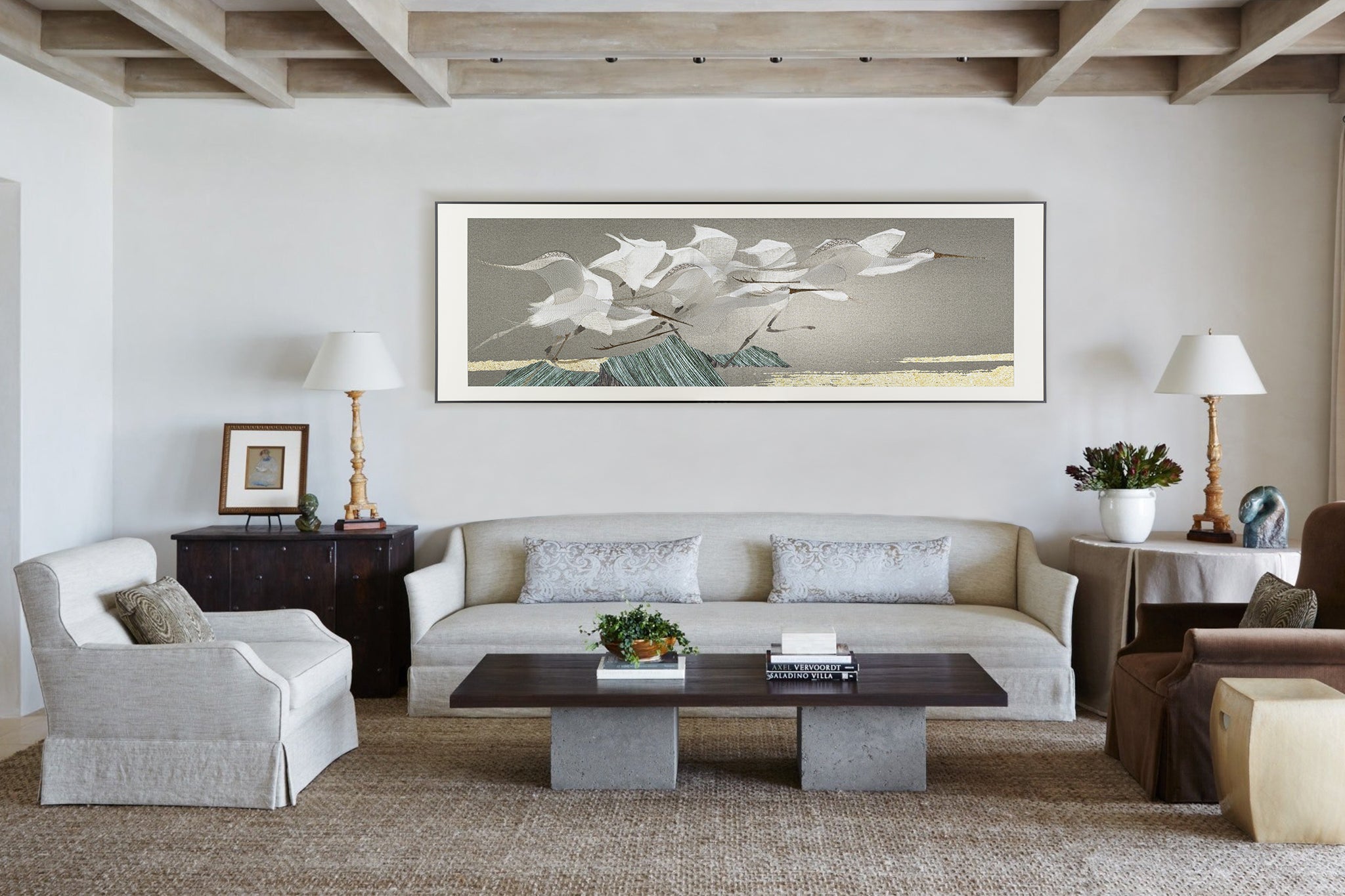 A large framed embroidery of an egrets design depicting herons in flight above the ocean, hanging on one wall of the living room, surrounded by contemporary furniture and stylish decorative items, creating a sophisticated atmosphere with neutral tones and soft lighting.