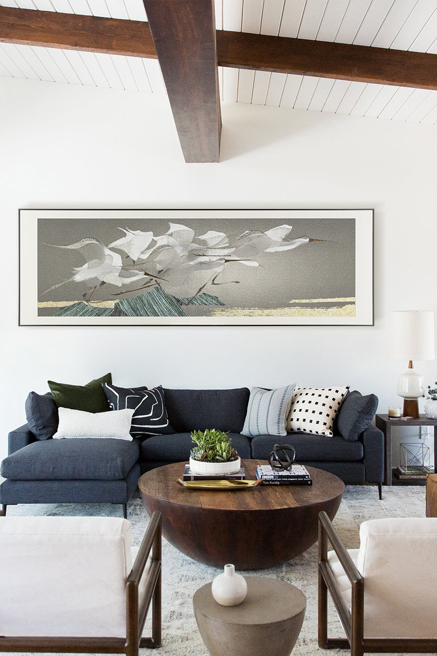 A large, horizontal embroidery art piece of egrets in flight above the living room&