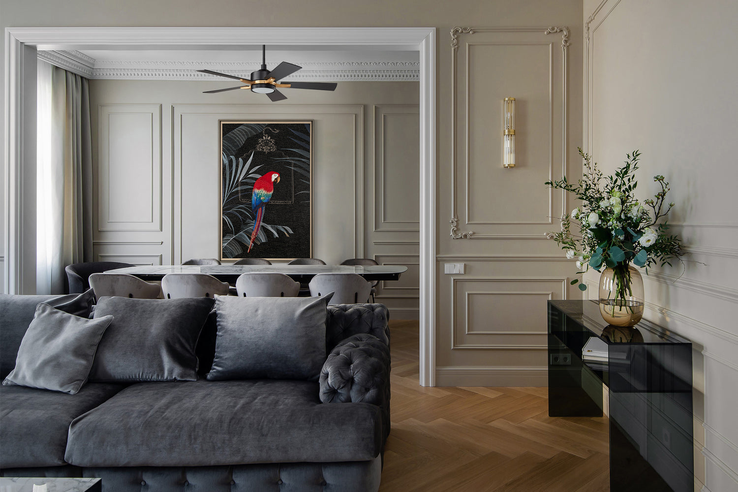 An framed embroidered artwork showing tropical parrots hangs on the dining room wall behind the living room. The black background in the painting is paired with a smart black ceiling fan with LED light, which makes the whole living room very luxurious.
