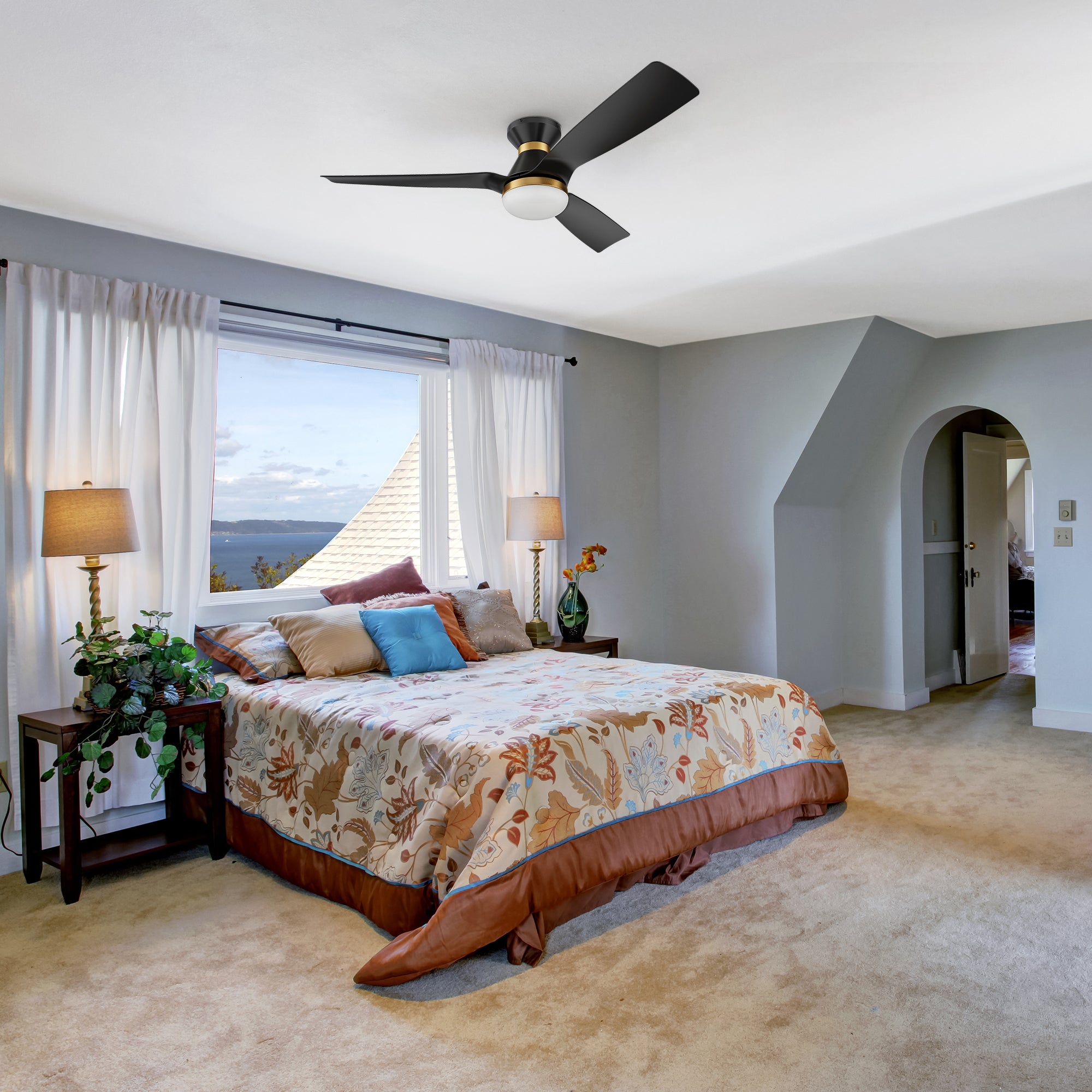 A modern bedroom featuring a Livex Black & Gold 52-inch Low Profile Smart Ceiling Fan with LED light and remote, mounted on a white ceiling for efficient airflow and cooling.  The ceiling fan has black blades with gold accents, complementing the room&