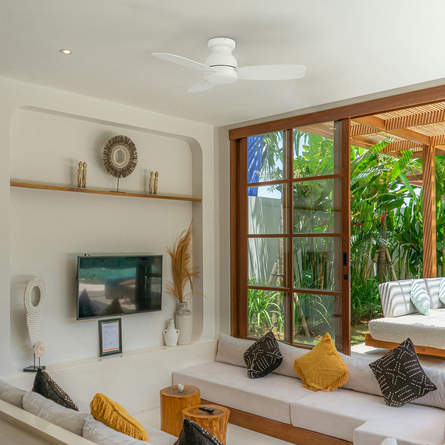 Osborn 44-inch white low profile ceiling fan mounted in a bright living room with tropical plants, large windows, and a cozy seating area.