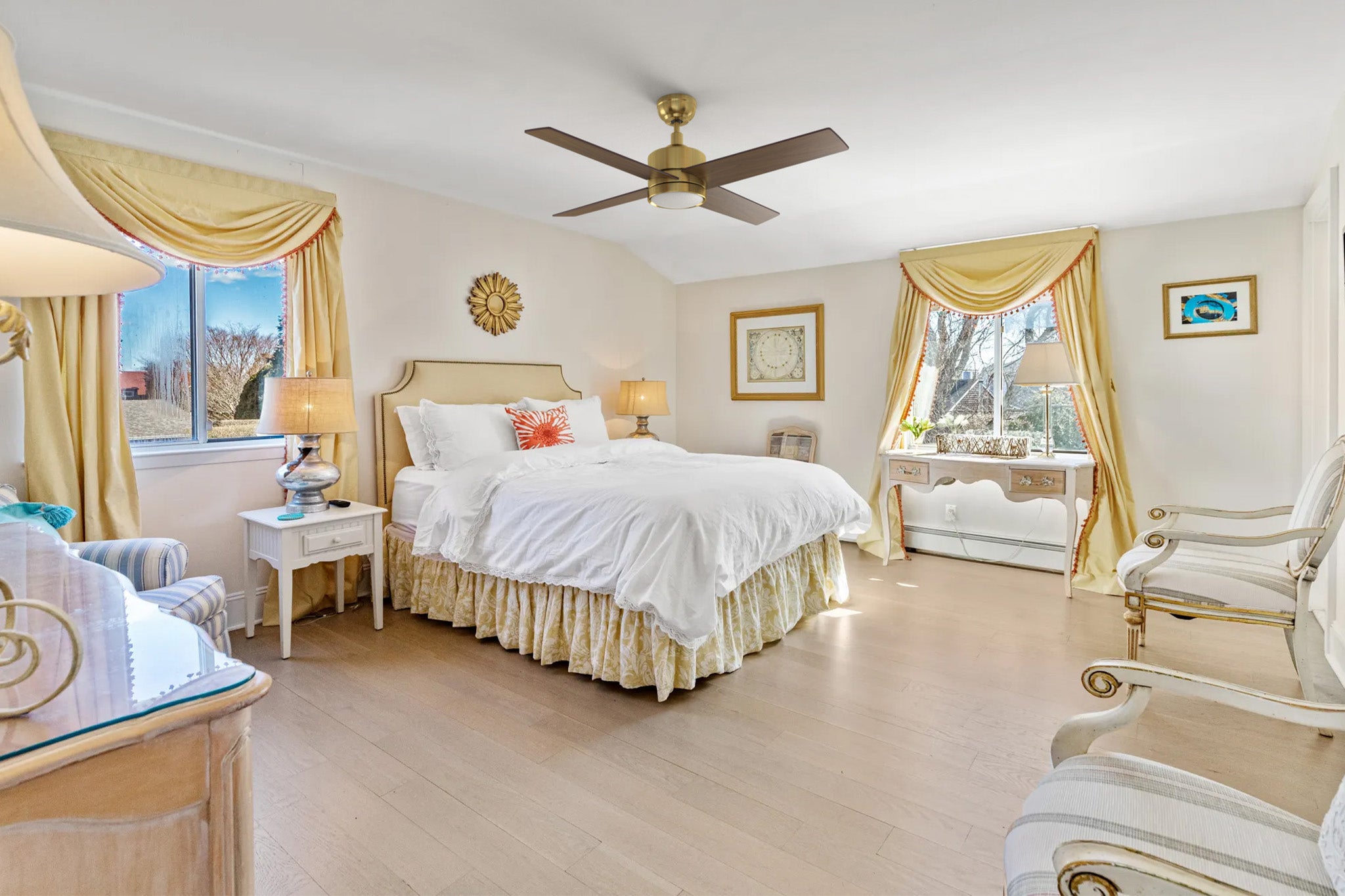 A 52-inch Rossendale traditional ceiling fan with LED light, featuring a black body with four wooden blades, mounted on a white ceiling in a bedroom. The fan includes a white frosted glass light fixture, positioned above a wooden bed with a white comforter and pillows, flanked by two nightstands with lamps, with carpeted flooring and a window with curtains.
