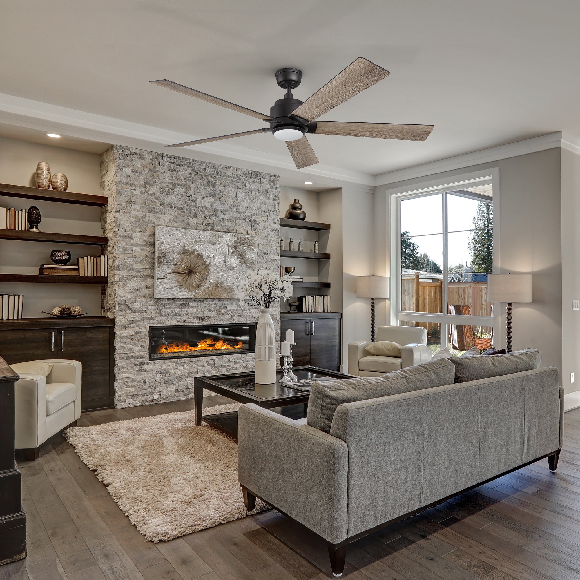 Modern living room featuring the Smafan Carro Aspen 60-inch ceiling fan with matte black hardware and wood-tone blades, elegantly complementing a gray stone fireplace, built-in shelves, and contemporary furniture in neutral tones.