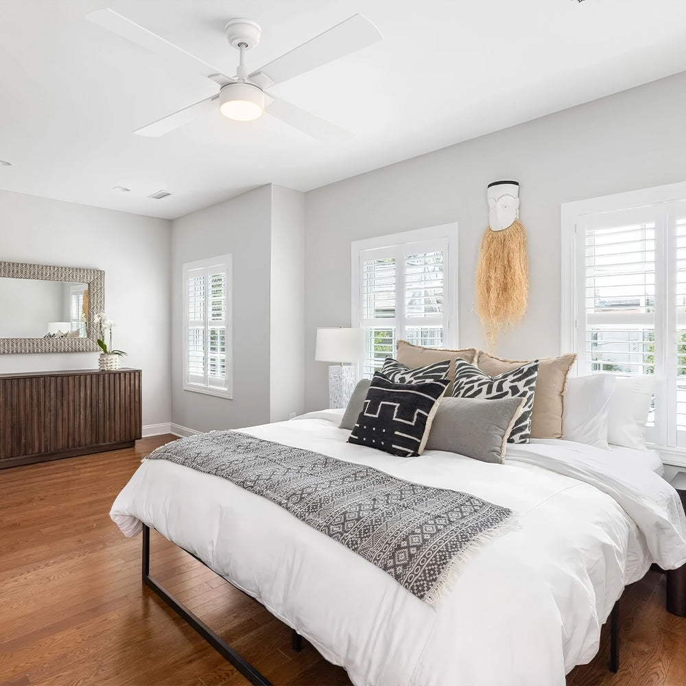 White Smafan Admiral 52-inch ceiling fan with light installed on a bedroom ceiling, featuring a large bed with white bedding, patterned pillows, and hardwood floors.