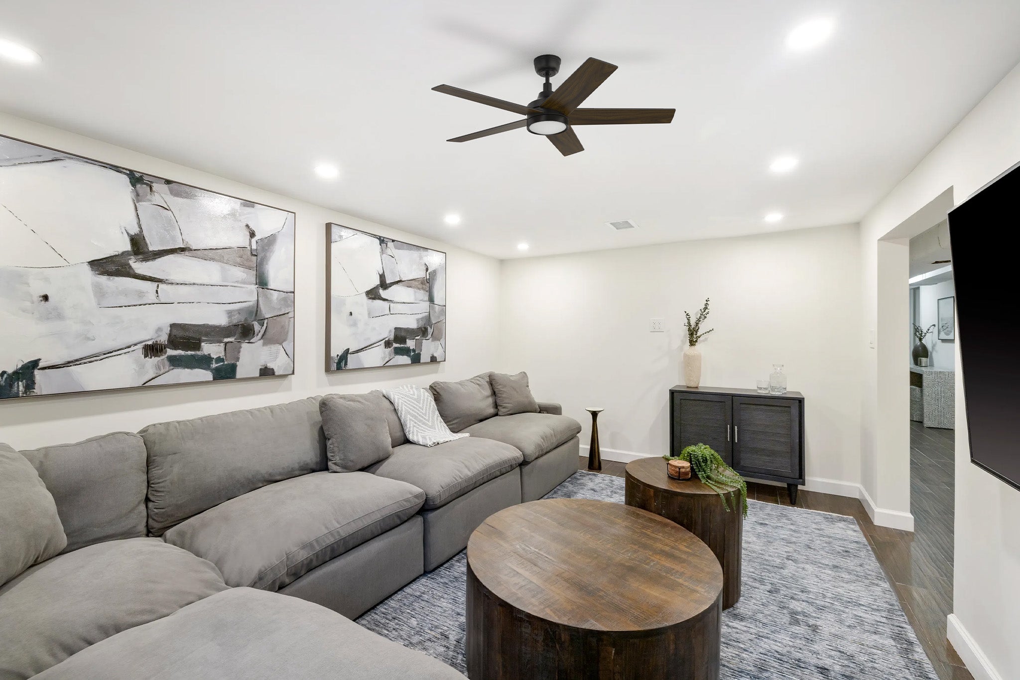 Albi Modern black ceiling fan with LED light displaying a sleek minimalist profile, mounted on a white ceiling with recessed lights alongside abstract wall art panels.