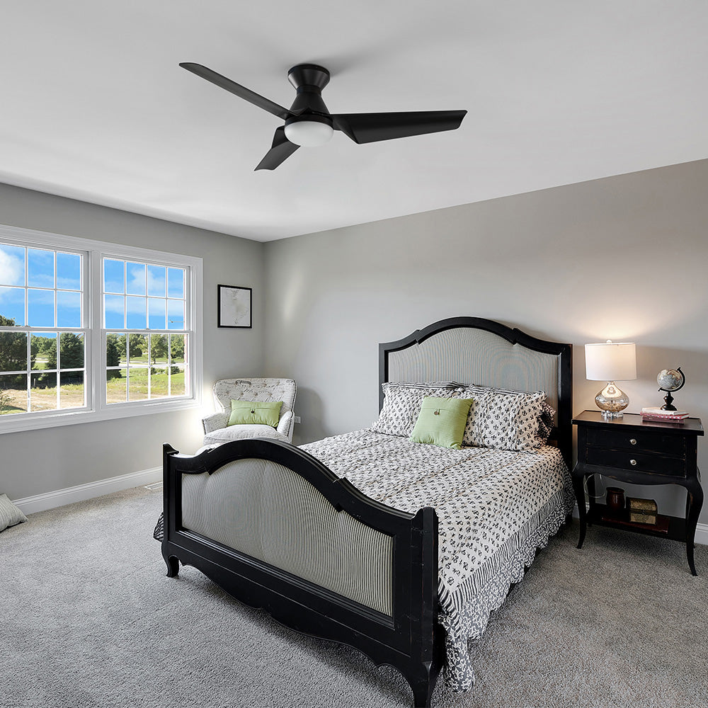 Modern bedroom with gray carpet and light gray walls, featuring a black bed frame, large windows, and a black three-blade ceiling fan with integrated light.