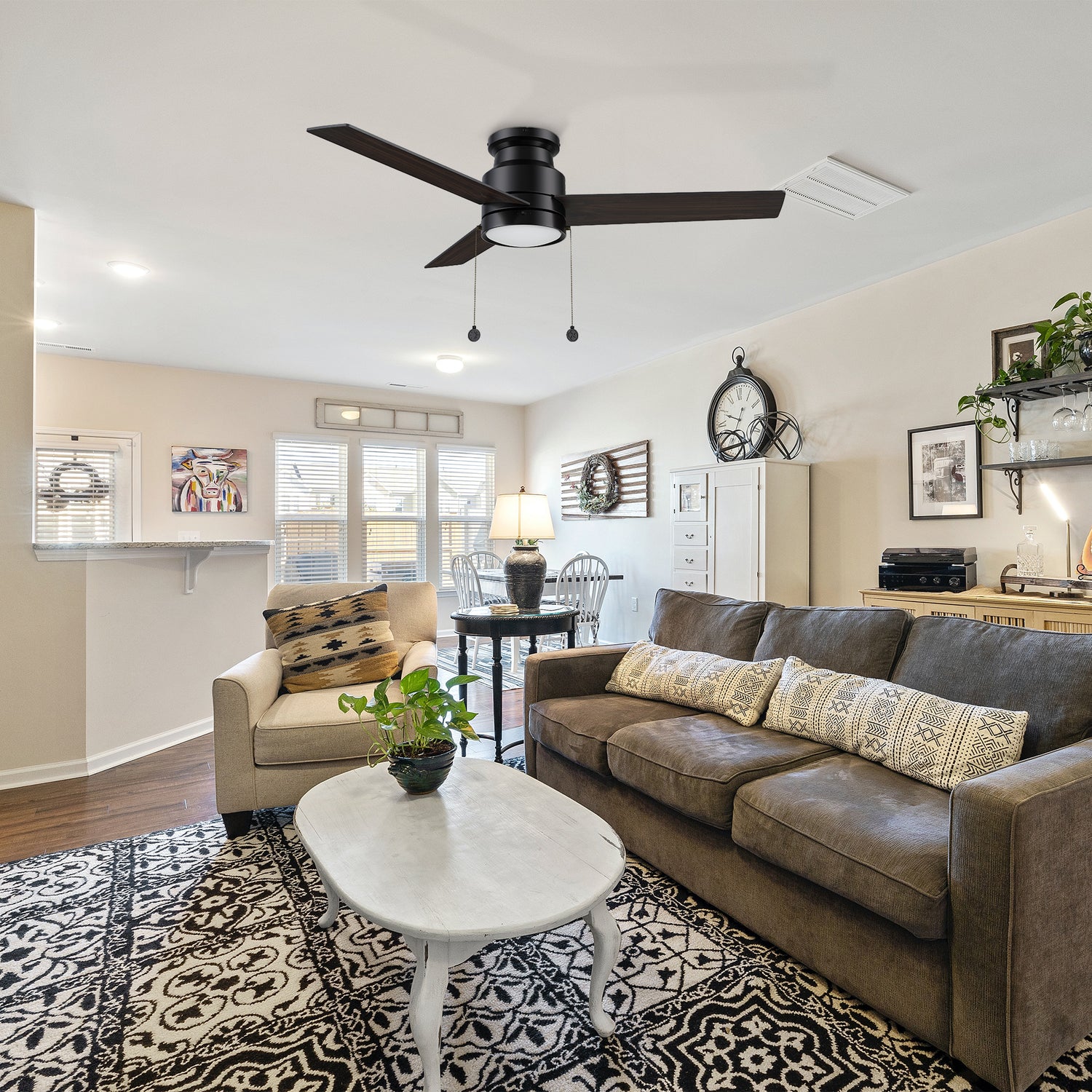 Black flush mounting ceiling fan with led light, matches with brown three-person sofa, ivory and white wooden coffee table, large carpet with black and white pattern, vintage clock and abstract murals make the living room design very artistic.