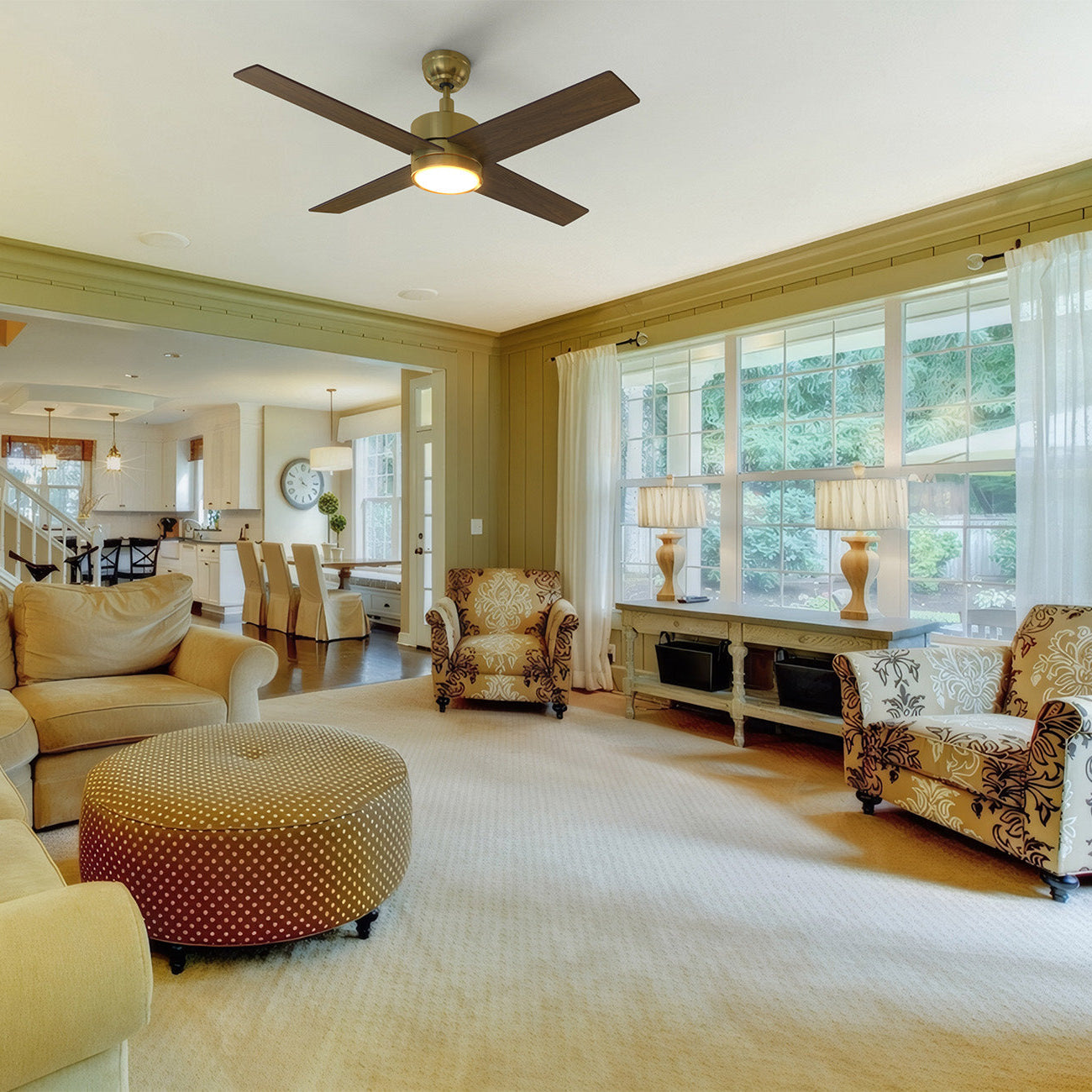 Modern living room featuring a Smafan Rossendale 52-inch gold ceiling fan with integrated bright LED light, beige sectional sofa, patterned armchairs, round ottoman, and large windows with sheer curtains allowing natural light.