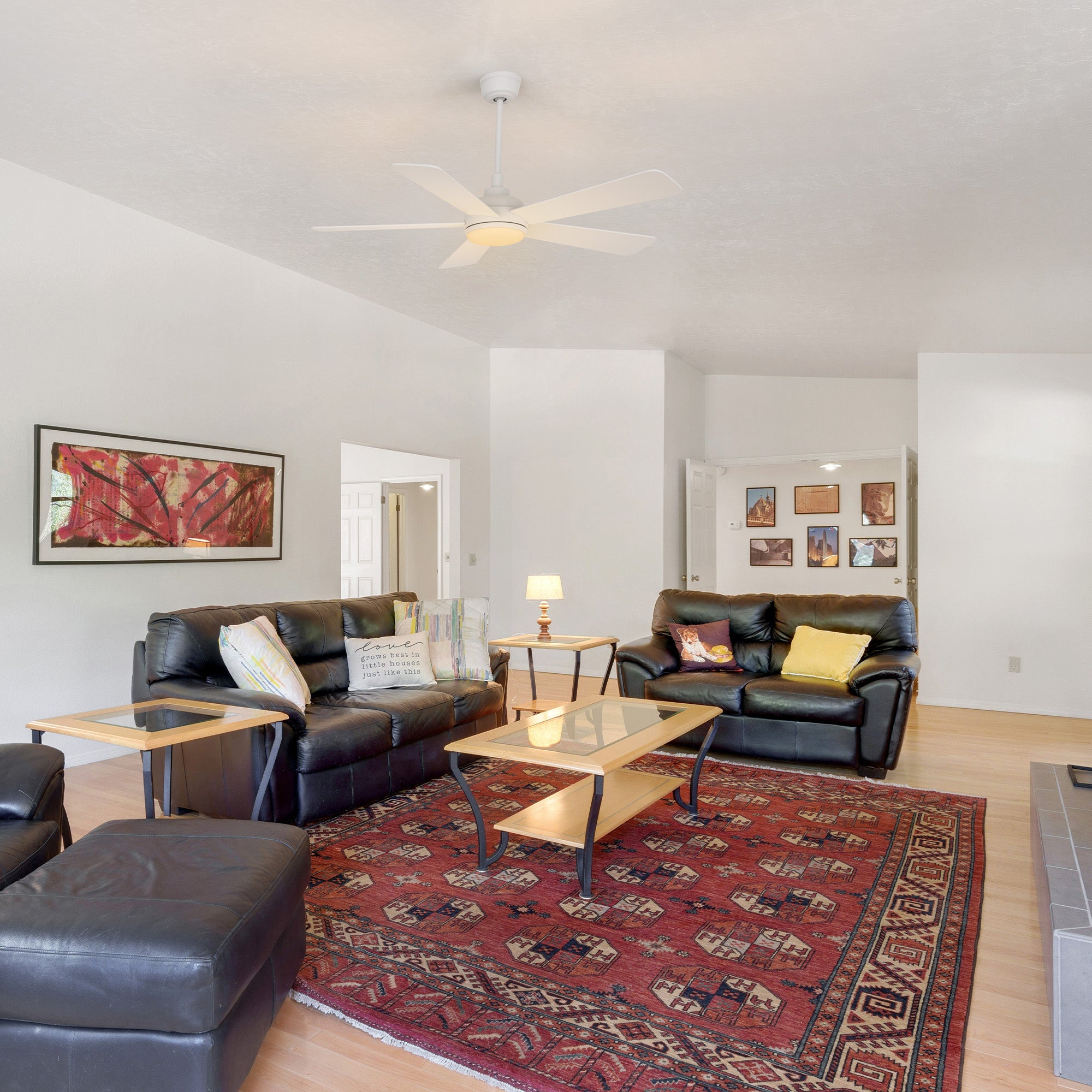 Smafan Toplam 52 inch white ceiling fan with LED light installed in a traditional living room featuring black leather sofas, a glass-top coffee table on a red and blue patterned rug, and wall artwork, creating a bright and inviting space with both style and comfort.