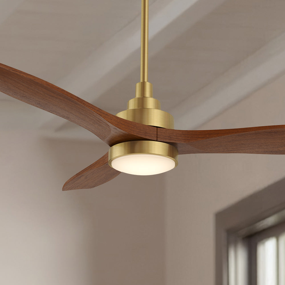 A close-up view of a Smafan Ultiem 48-inch ceiling fan featuring a gold motor hub, downrod, and a circular white LED light, paired with three curved walnut finish solid wood blades. The fan is mounted on a white ceiling, with a wall and window in the background.