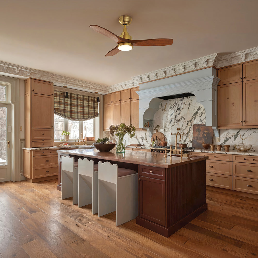 A kitchen with light wood cabinets and a dark wood island, featuring a Smafan Ultiem 48-inch solid wood ceiling fan in gold finish with LED light, and a marble backsplash behind the stove.