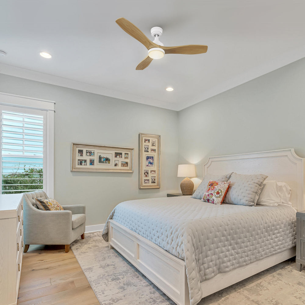 French-country bedroom with upholstered bed, soft linens, framed art, and bedside lamps; ceiling fitted with Ultiem 48-inch light-wood fan and integrated LED providing gentle ambient lighting.