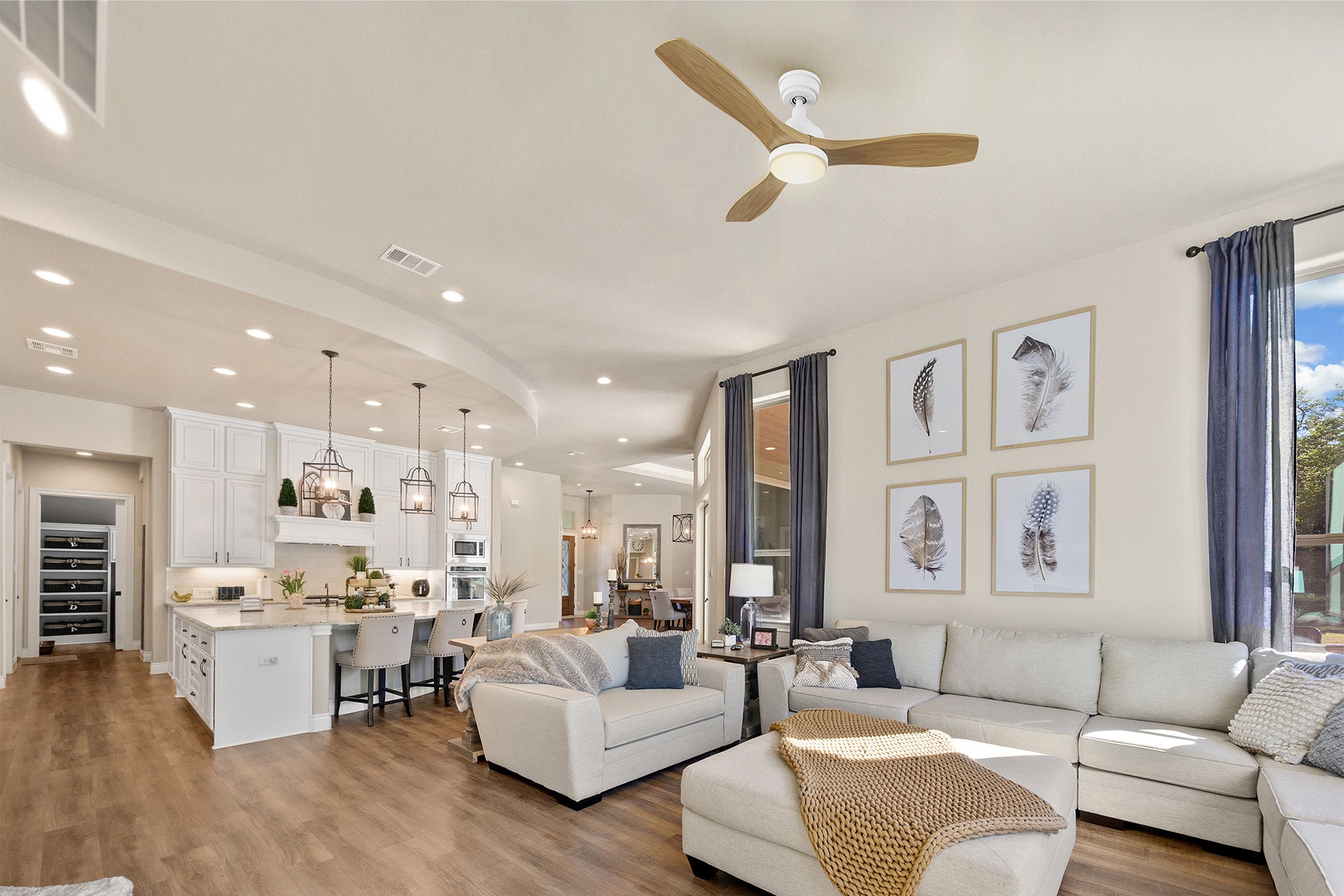 Smafan Ultiem 48 inch ceiling fan with LED light and remote, featuring light wood blades in a Scandinavian style living room with beige sectional sofa, modern kitchen, and feather-themed wall art.