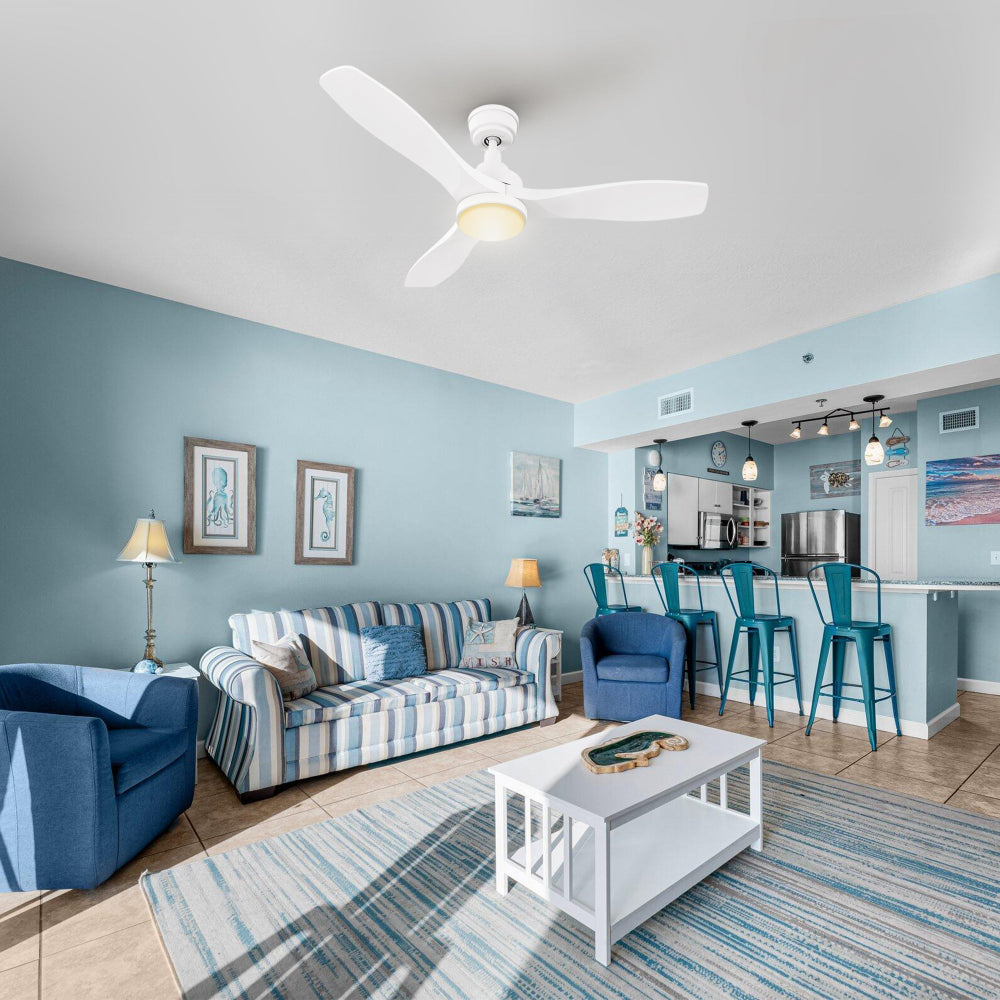 Coastal-traditional living room with blue-and-white textiles, wood coffee table, and framed art; Ultiem 48-inch white fan with integrated LED mounted overhead for bright, even airflow.
