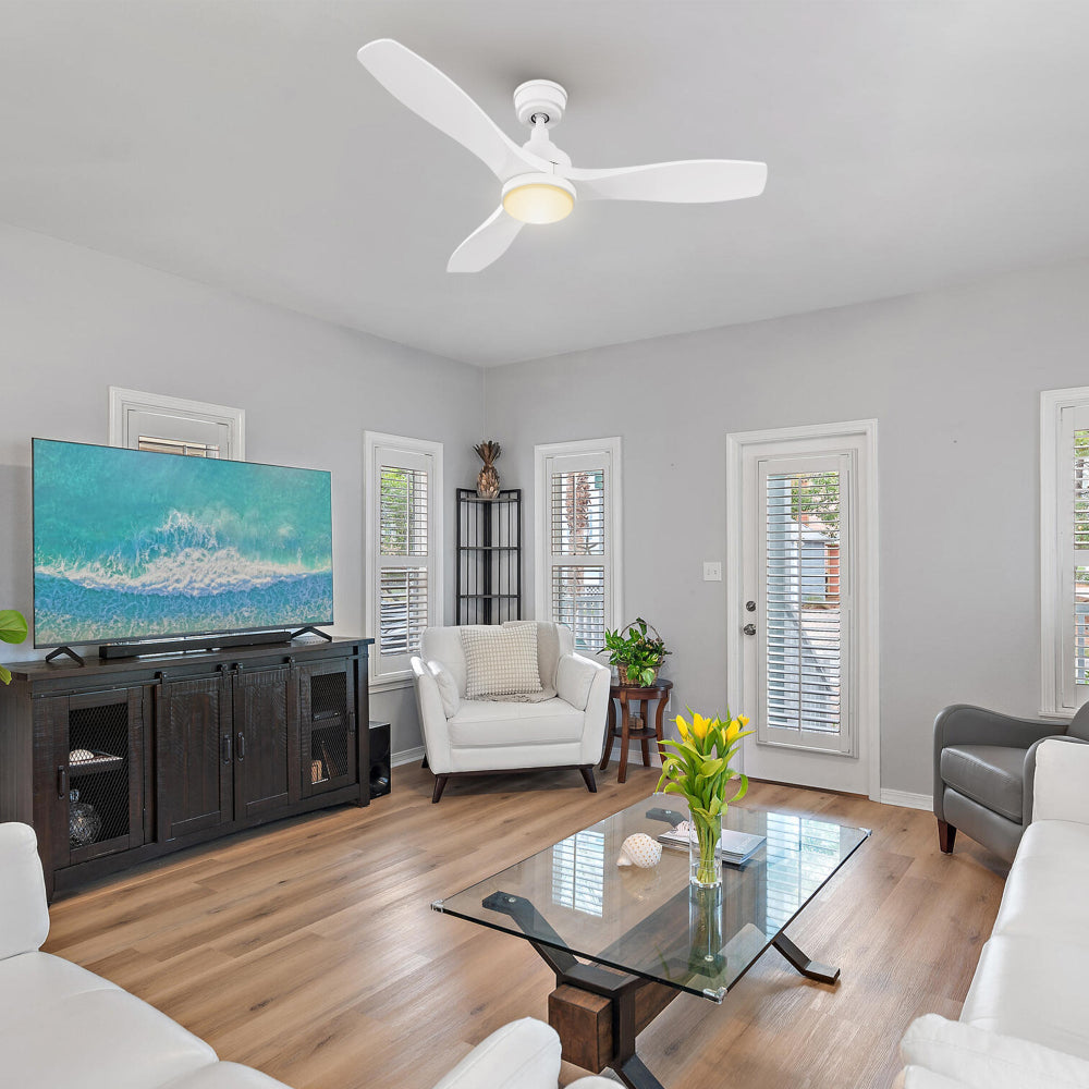 Modern living room with TV console, accent chair, and tall windows; Ultiem 48-inch white fan with round LED light centered above seating to deliver bright illumination and smooth airflow.