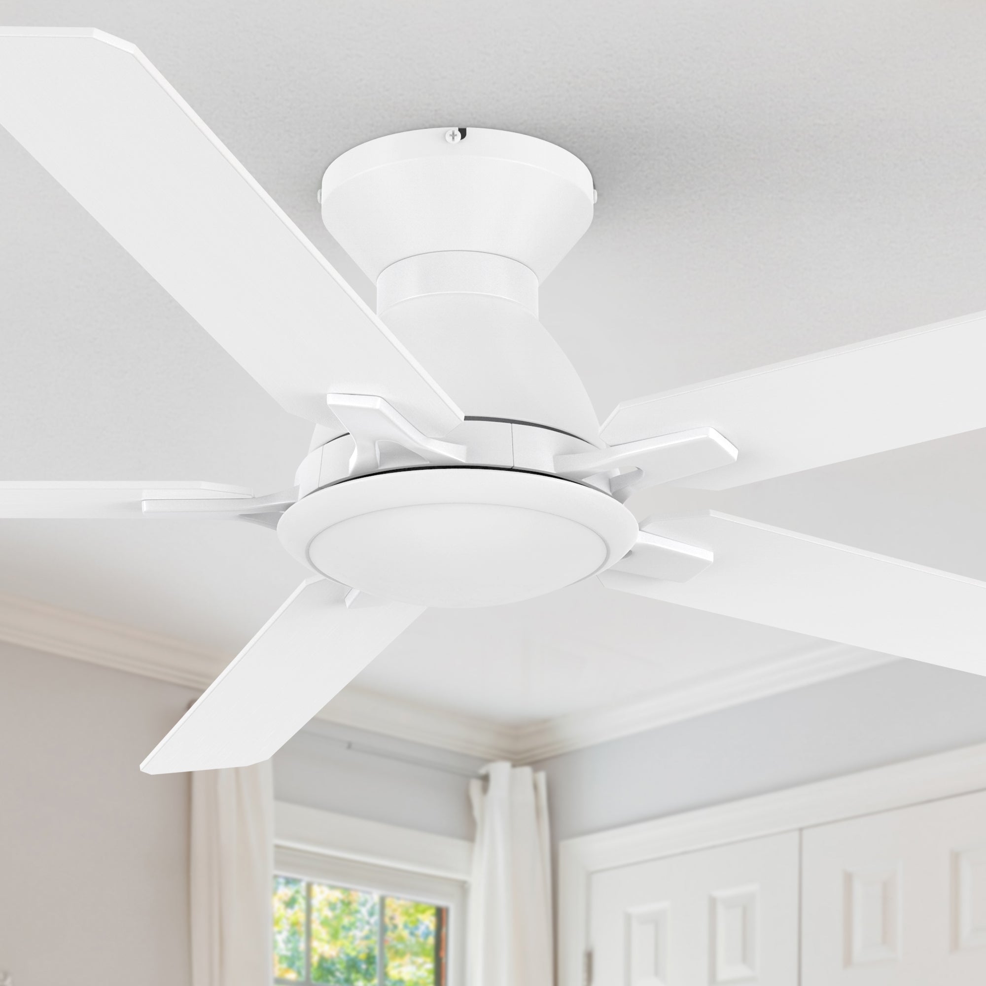 A white, five-blade, low-profile ceiling fan with an integrated LED light kit is installed on a white ceiling in a room with a window and a white paneled door.