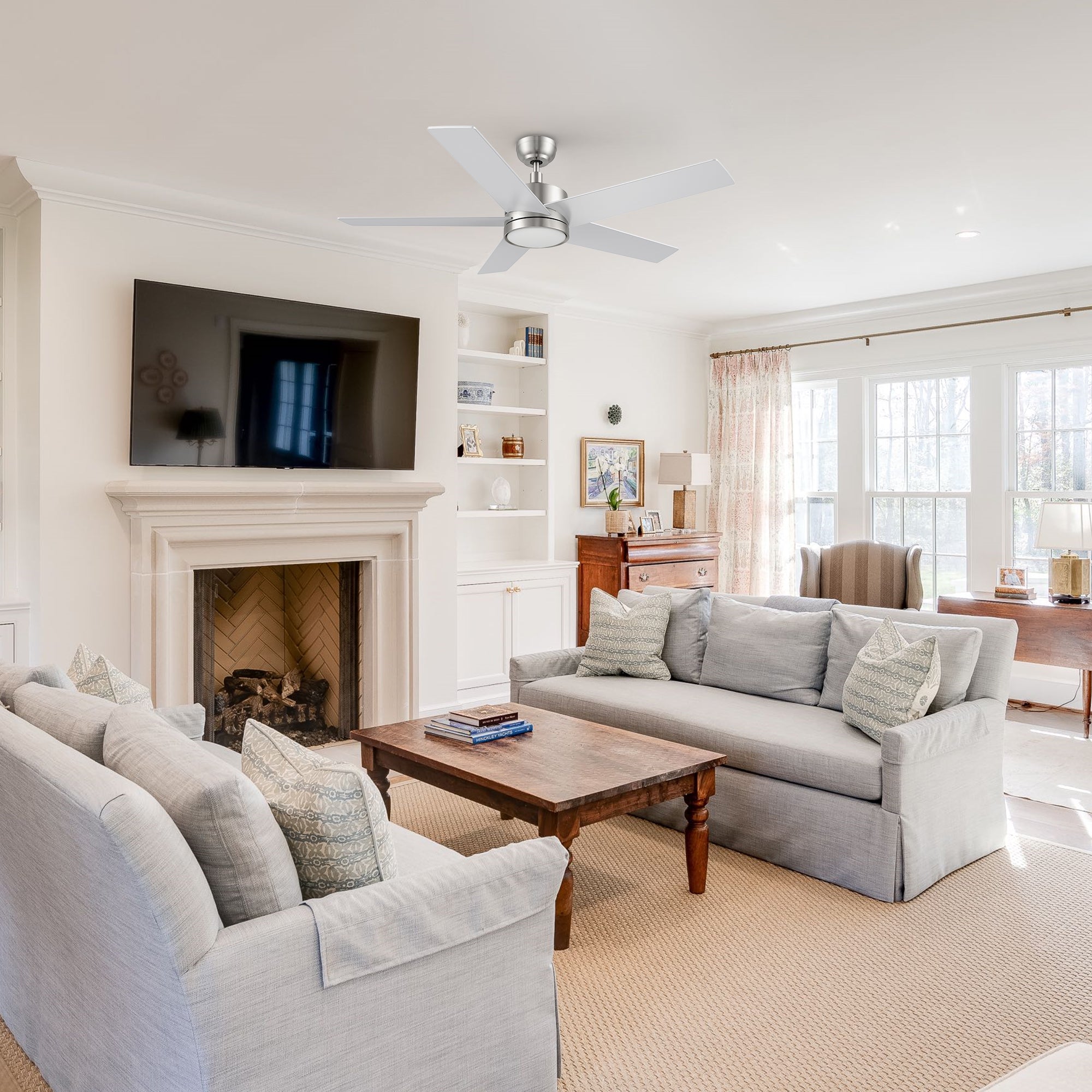 Traditional living room with soft neutral tones, featuring two gray sofas, a wooden coffee table, fireplace with a TV above, and the Smafan Trafford 52-inch brushed nickel ceiling fan with light mounted on the white ceiling.
