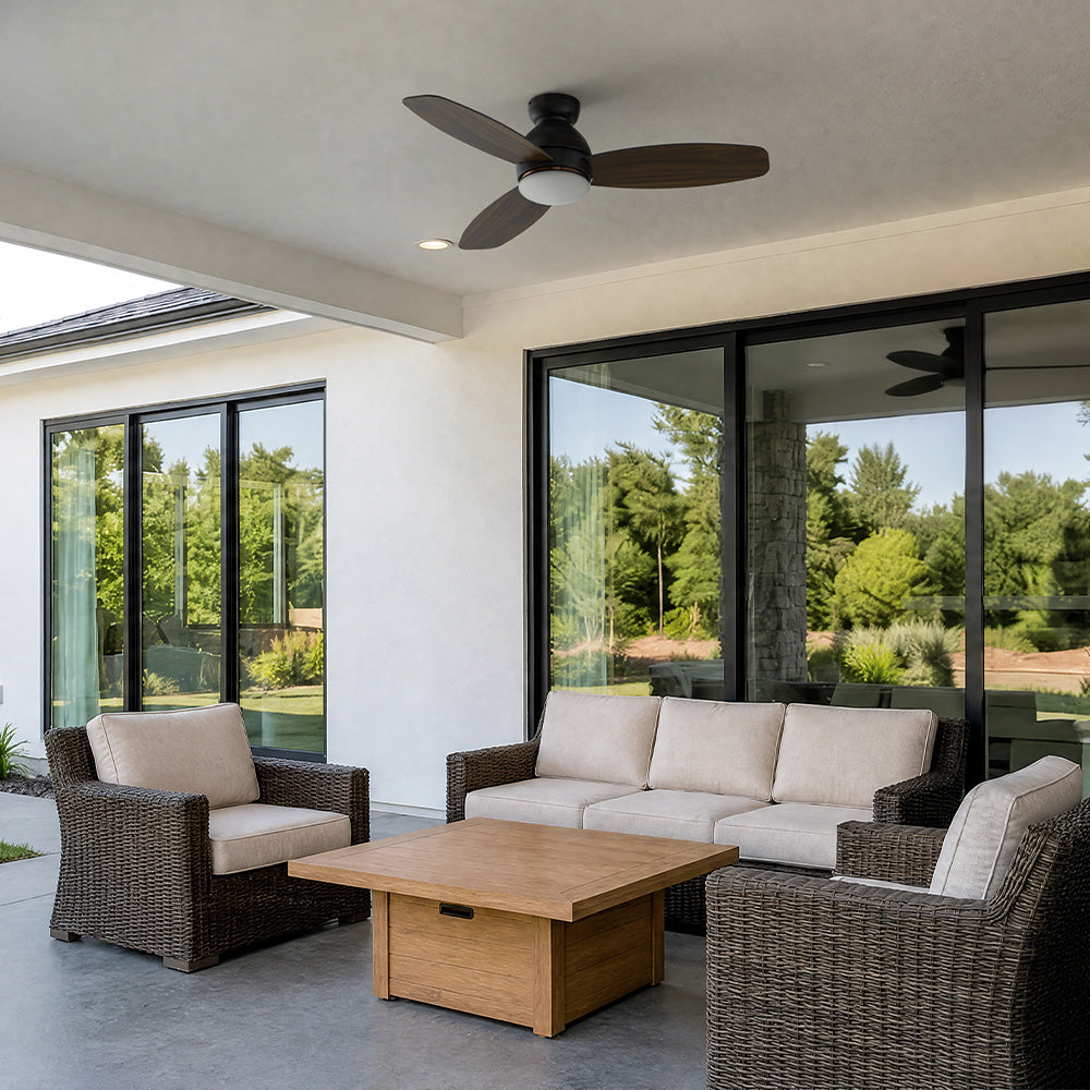 Carro Bretton 48 inch low profile outdoor ceiling fan with dimmable light kit installed on a covered patio lounge area with wicker seating and sliding glass doors.