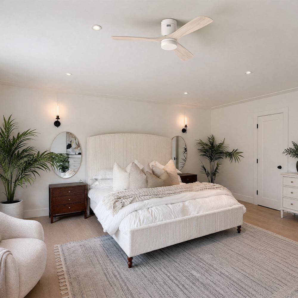 Smafan Alfa 52 inch solid wood flush mount ceiling fan installed in a modern minimalist bedroom. The low profile ceiling fan features natural wood blades and a clean white finish, complementing the neutral bedroom décor with a textured upholstered bed, indoor plants, warm lighting, and contemporary coastal-inspired style.
