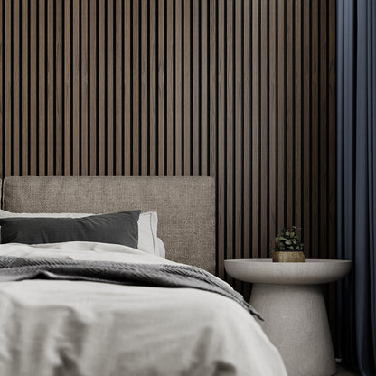 American Dark Walnut Acoustic Slat Wood Wall Panel installed behind a cozy bed setup with neutral bedding and a round side table, creating a warm and relaxing bedroom ambiance.