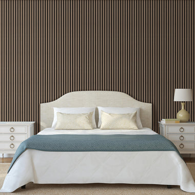 Modern bedroom featuring a wall covered with American natural walnut acoustic slat wood panels with black felt, complemented by a bed with white linens and a blue throw blanket, along with a bedside lamp and cabinet.