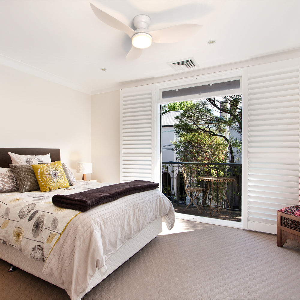Annecy 45-inch white flush mount ceiling fan with LED light installed in a cozy bedroom featuring natural light, balcony view, and modern decor. 