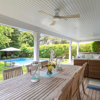 White flush mount wood ceiling fan with light installed on a white covered patio ceiling above a large wooden outdoor dining table with a backyard swimming pool view. 