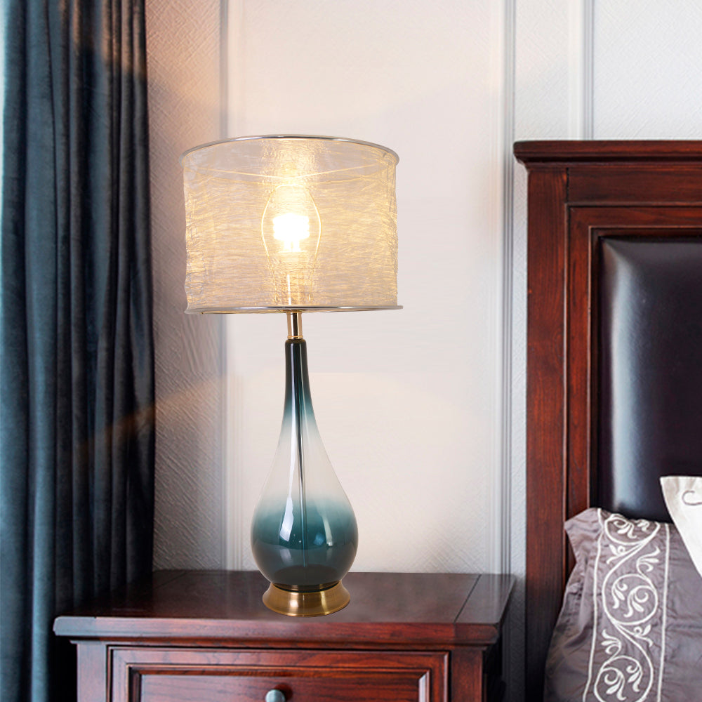 A bedroom view featuring two Carro Smafan 30-inch Tulip Big table lamps with Dark Green Ombre finish and Translucent Silver shades, placed on nightstands on either side of a bed. The lamps emit a warm glow, complementing the room&