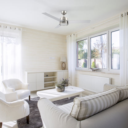Modern living room featuring the Carro Smafan 52-inch Louy ceiling fan in brushed nickel with integrated LED light, styled in a bright, neutral-toned living room with large windows, white furniture, and soft natural lighting. 