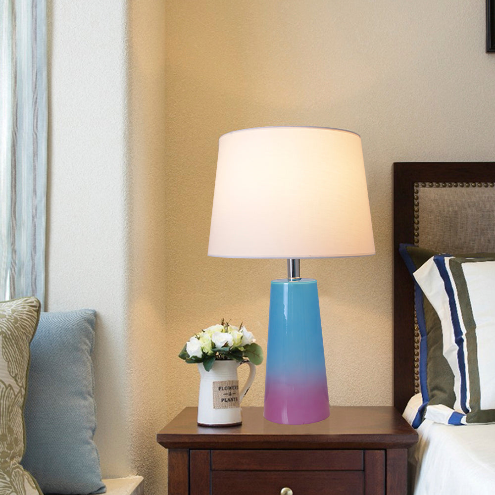 Carro Smafan Rosemary 25-inch table lamp with blue to purple ombre ceramic base and white lampshade placed on a wooden nightstand in a cozy, warmly lit bedroom. 