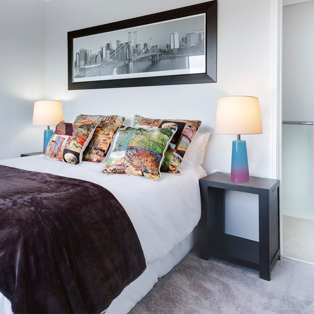 Matching pair of Carro Smafan Rosemary lamps on dark nightstands flanking a bed with floral pillows and a brown throw in a traditional bedroom setting. 