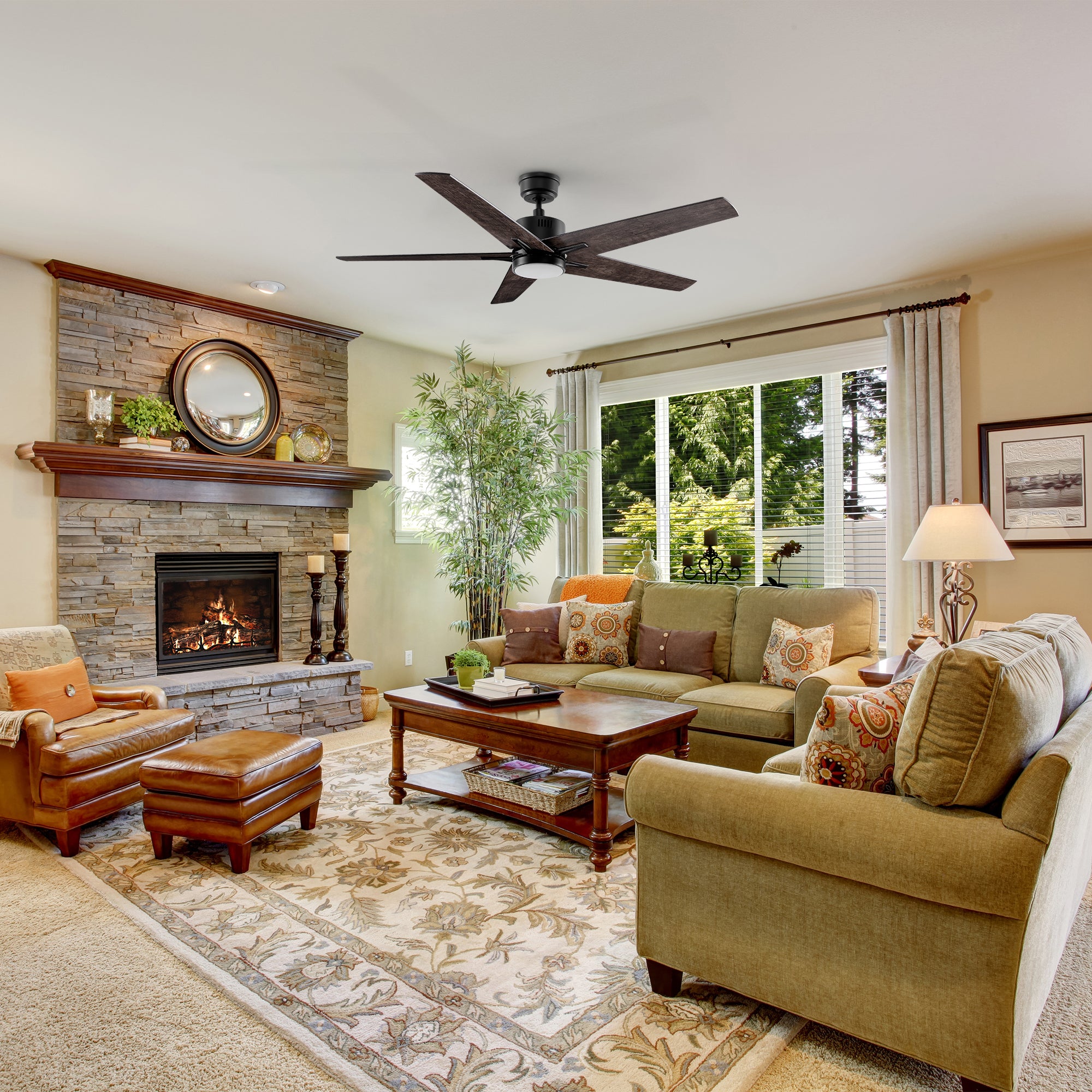 A 52-inch ceiling fan with a black finish and wood-grain blades, installed in a cozy living room with a fireplace, warm lighting, and wooden furniture. 