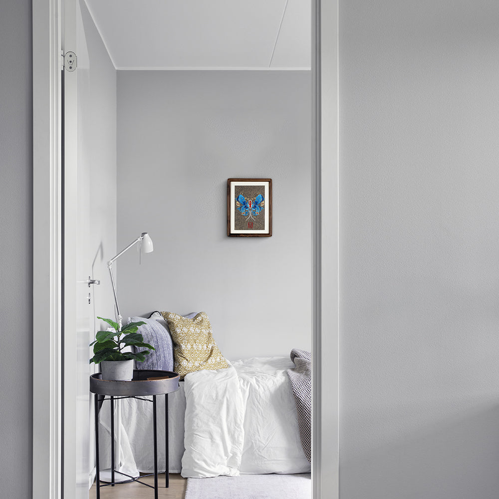 A wood-framed embroidered artwork showing beautiful blue butterfly, hangs on the white wall of the modern bedroom.