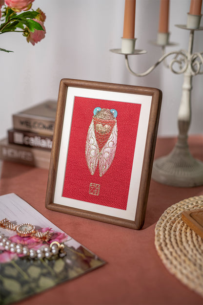 An embroidered artwork of cicadas, placed on a side table, is paired with champagne-colored candles, white candlesticks, jewelry, and pink flowers.