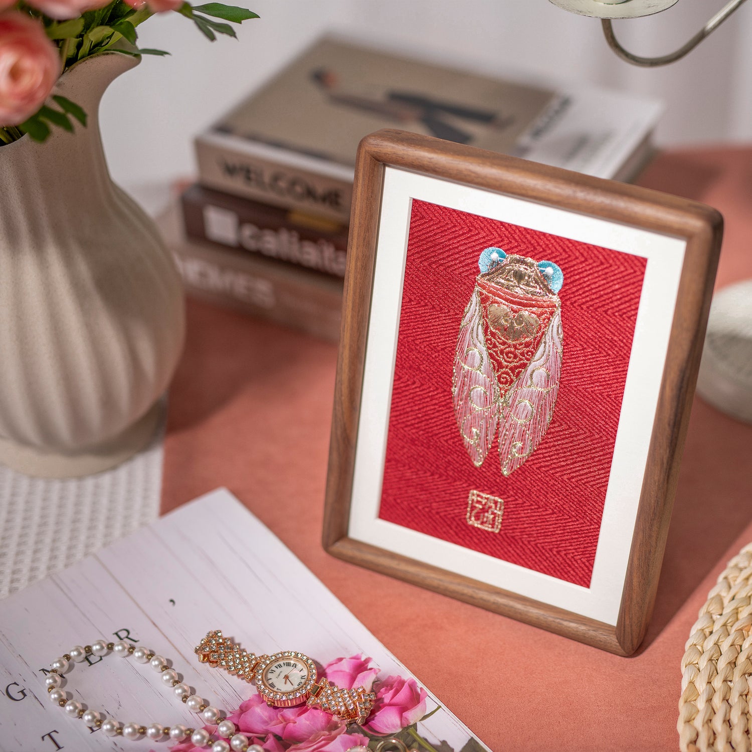 The embroidery artwork design of golden cicada placed on the table, matching to the pink flowers, pearl necklace and gold watch.