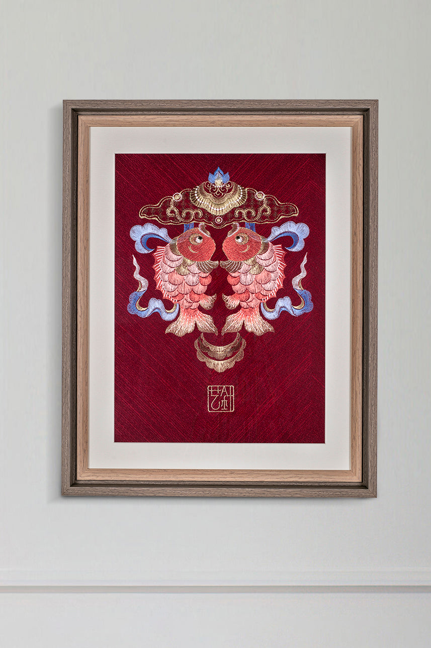 An embroidered artwork with two koi carp hangs on the wall as a home decoration.