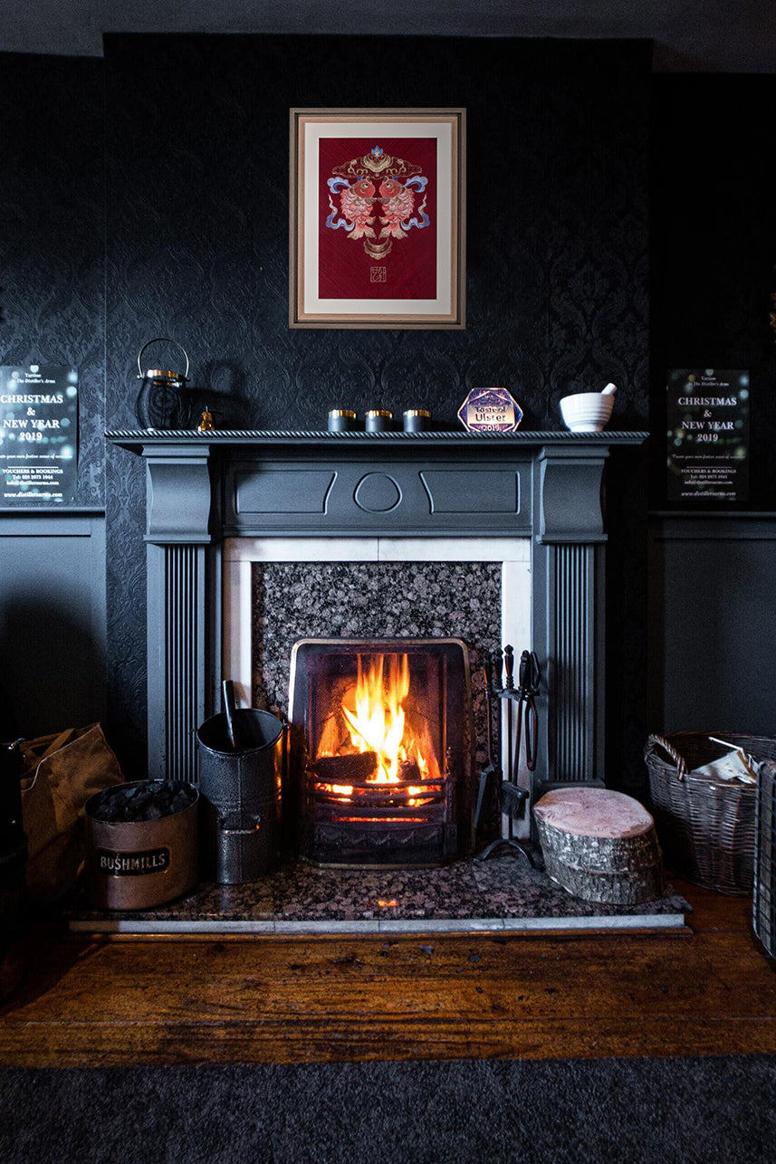In a dark, predominantly black living room, an embroidered work of art with double koi fish hangs over a wood-burning fireplace. The combination of red and black highlights the retro and elegant feeling of the whole living room.